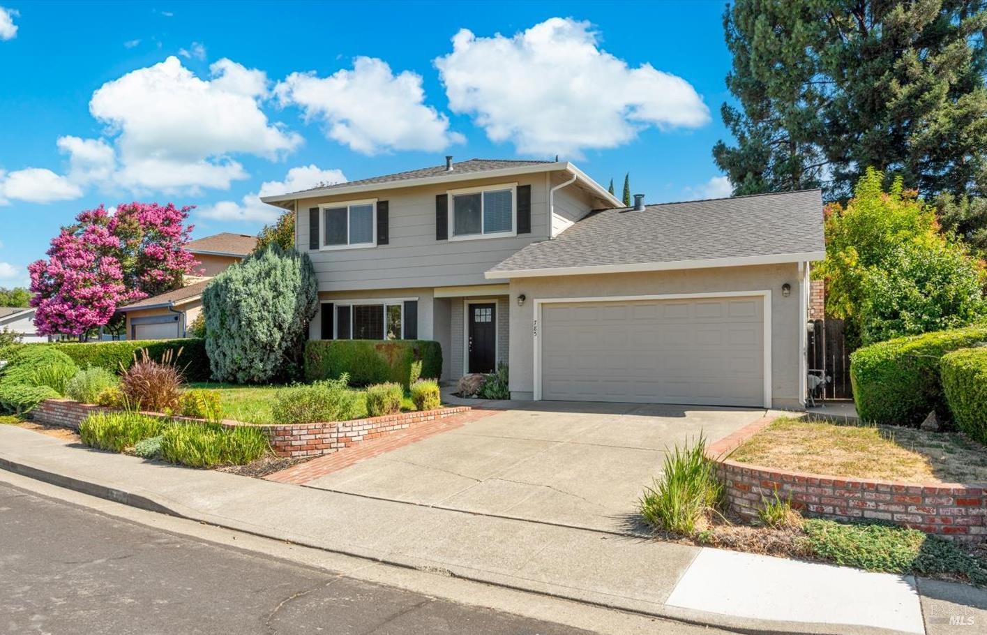 Two-story gray house with a wide garage, landscaped yard, and flowering pink tree.