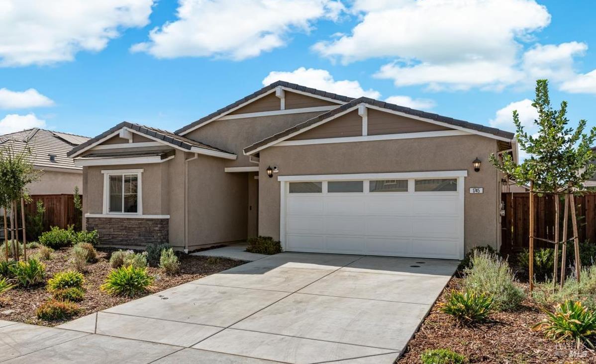 Single-story stucco home with a white two-car garage, broad driveway, and landscaped front garden.