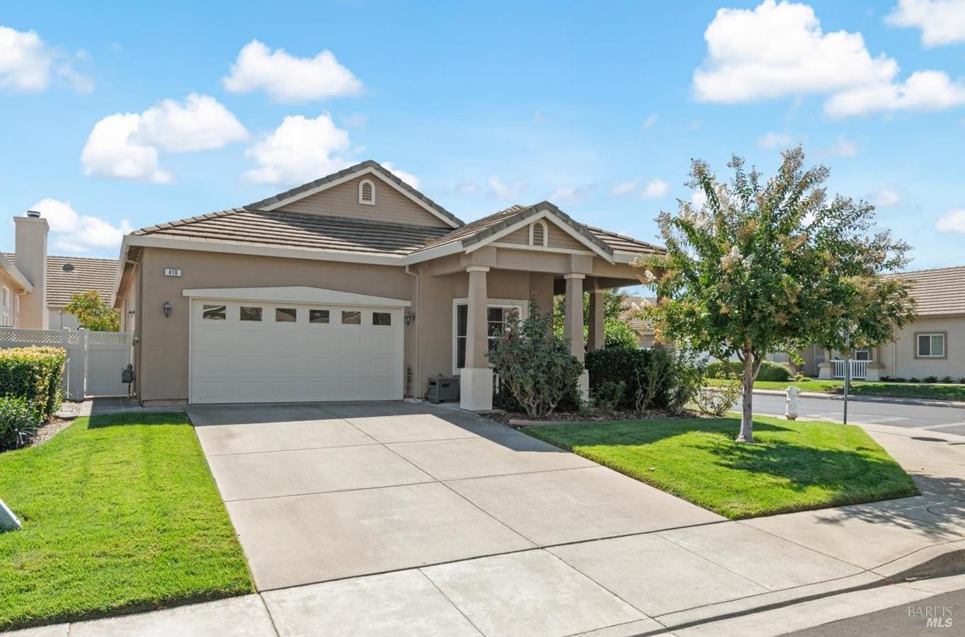 Beige single-story home with a two-car garage, covered entry, driveway, and landscaped front lawn.