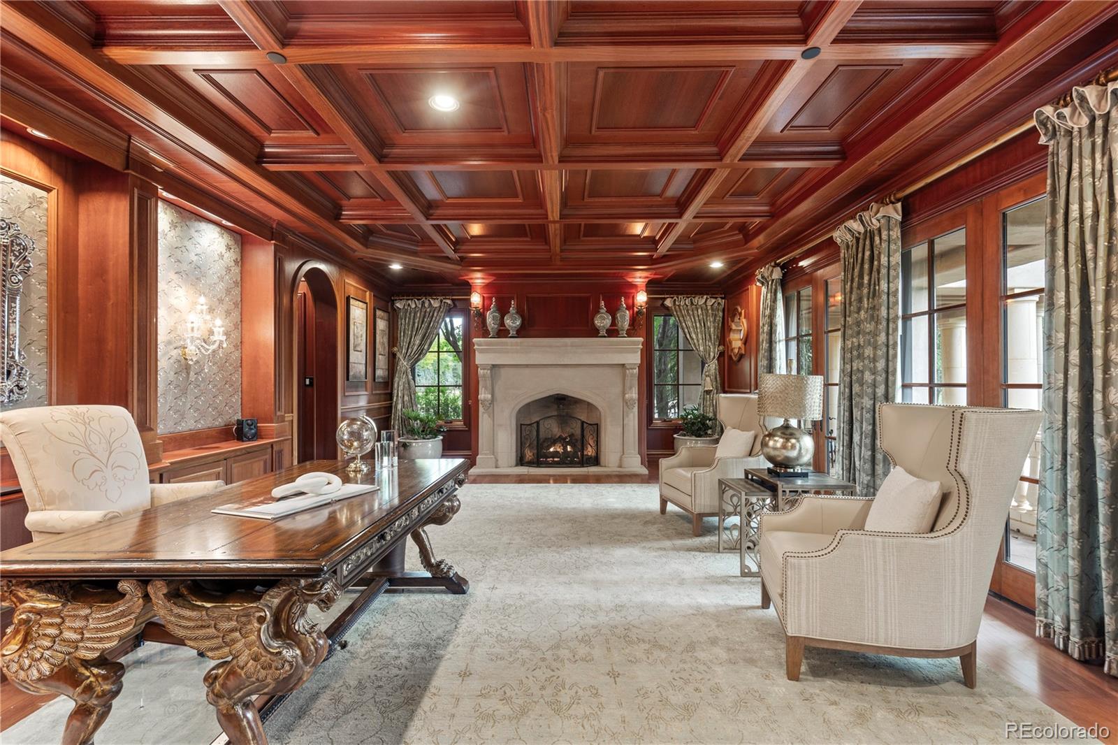 Formal living room with a stone fireplace, elaborate wood ceiling, and cream seating.