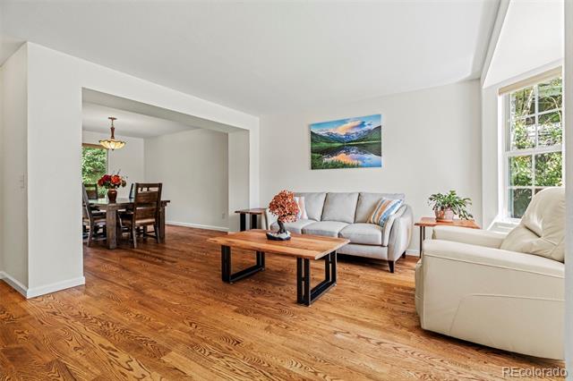 Living room with hardwood floors, gray sofa, cream armchairs, and an adjoining dining area.