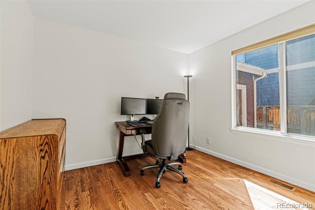 Home office with a dark wood desk, rolling chair, hardwood floors, and a large window.