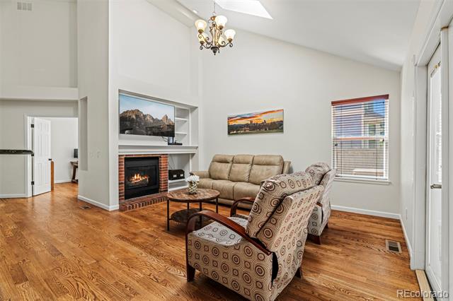 Living room with brick fireplace, vaulted ceiling, skylight, and hardwood floors.