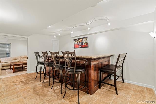 Basement bar with a dark wood counter, tall chairs, and tan tile flooring.