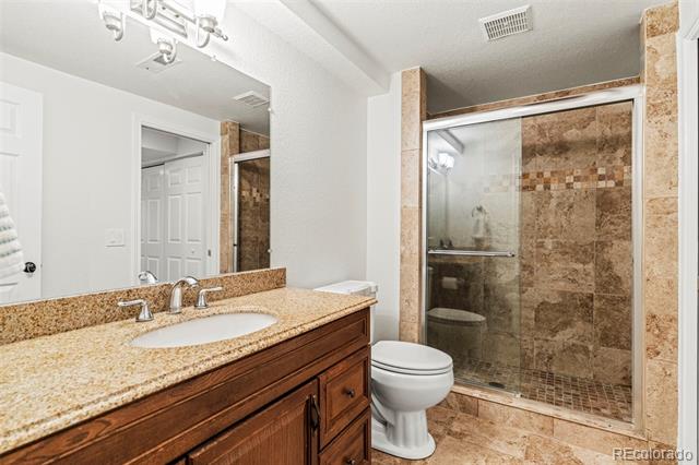 Bathroom with a wood vanity and stone countertop beside a glass-enclosed stone-tile shower.