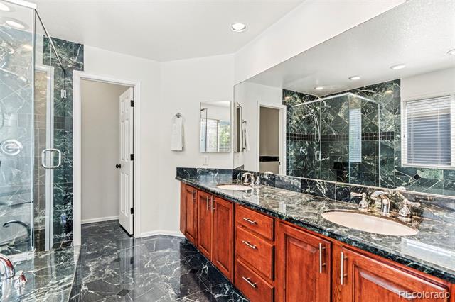 Bathroom with a reddish wood double vanity, dark marble surfaces, and a glass-enclosed shower.