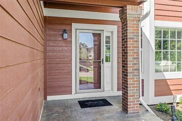 Covered home entrance with a glass storm door, brick column, and tiled porch.