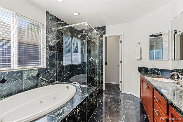 Bathroom with a jetted soaking tub, glass shower, and dark veined stone finishes.