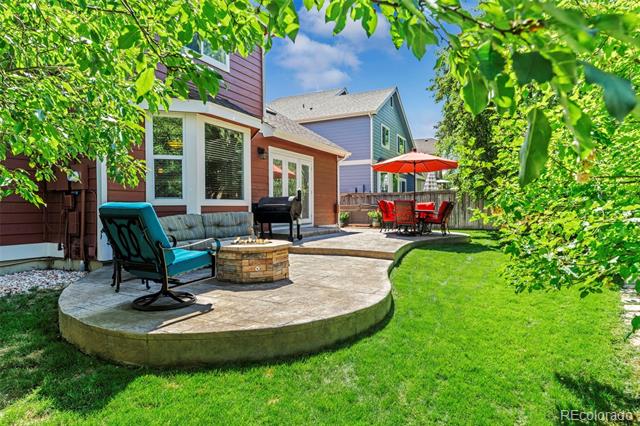 Backyard patio with a raised curved seating area, lounge chairs, fire pit, and red umbrella over a dining set.
