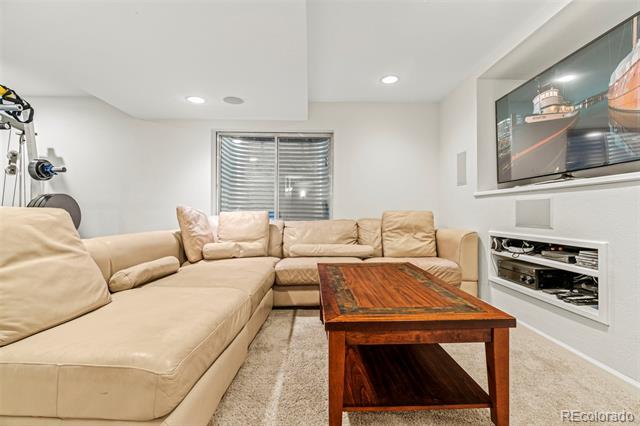 Basement family room with a beige sectional, wooden coffee table, and television above built-in media equipment.