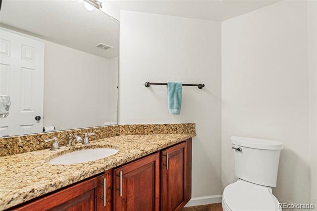 Bathroom with a granite vanity, wood cabinets, large mirror, and toilet.