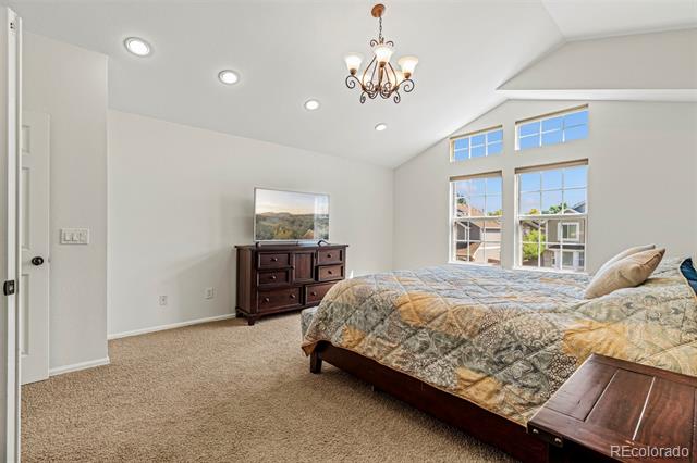 Bedroom with a large patterned bed, tall windows, and a dark wood dresser beneath a vaulted ceiling.