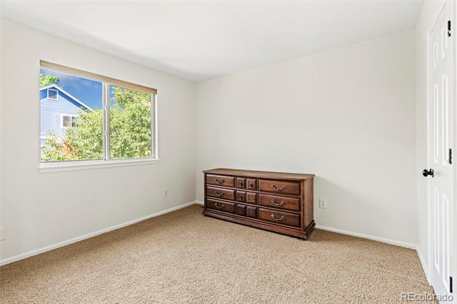 Carpeted bedroom with a wooden dresser and window overlooking trees.