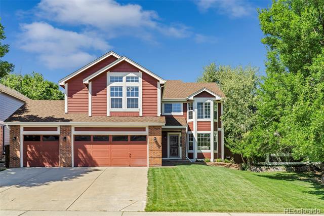 Two-story red-and-brick home with a three-car garage, broad driveway, and green lawn.