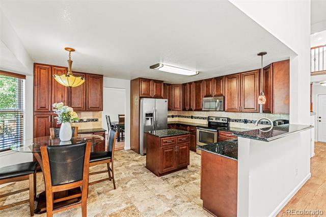 Kitchen with reddish wood cabinets, granite counters, stainless steel appliances, and a central island.