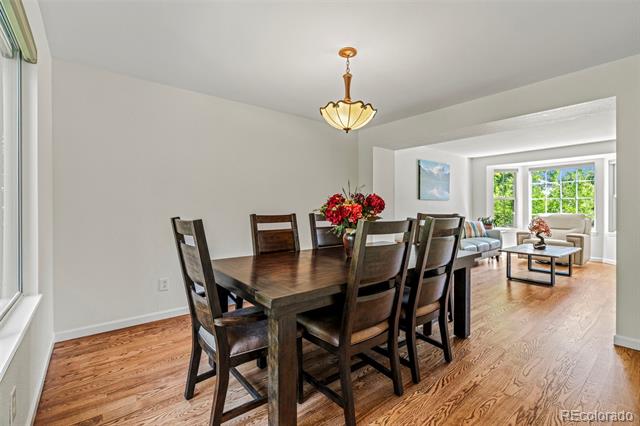 Dining room with a dark wood table and chairs, opening to a bright living area with large windows.