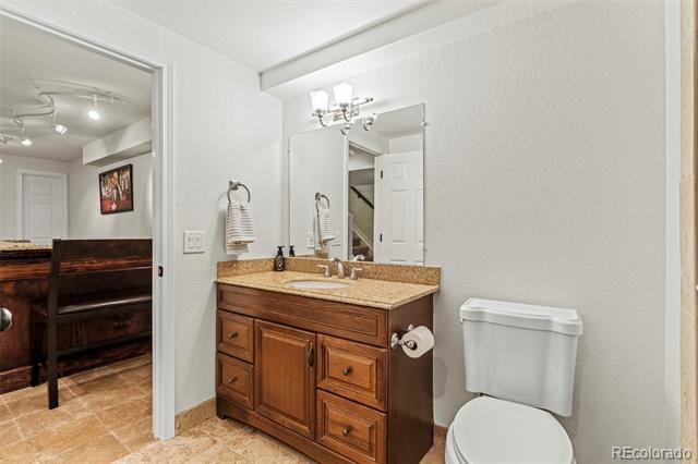 Bathroom with a dark wood vanity, tan countertop, and white toilet beside an open doorway.