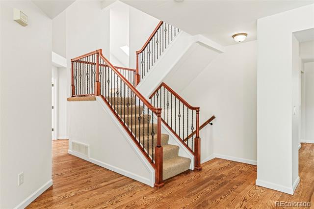 Foyer with a carpeted staircase, reddish wood railings, black metal balusters, and hardwood flooring.