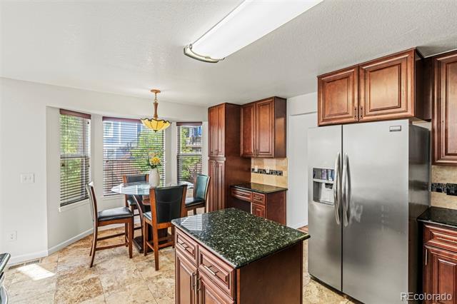 Kitchen with a dark granite island, stainless steel refrigerator, and sunny breakfast nook.