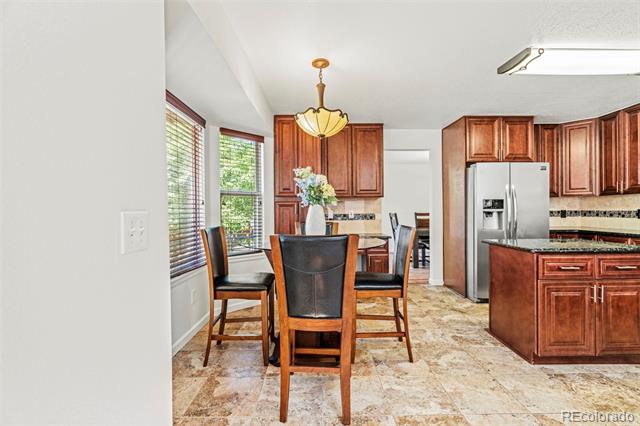 Dining area with a wood table beside a kitchen with reddish cabinetry and stainless steel appliances.