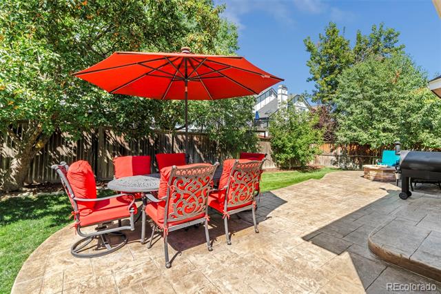 Back patio with a red umbrella, matching chairs, stone paving, and a fenced grassy yard.