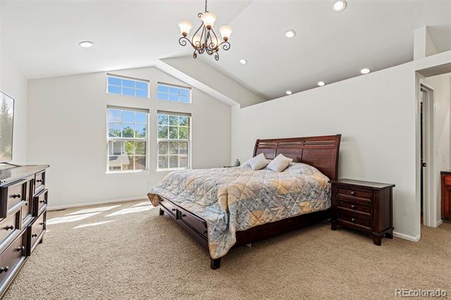 Furnished bedroom with a vaulted ceiling, chandelier, and tall windows.