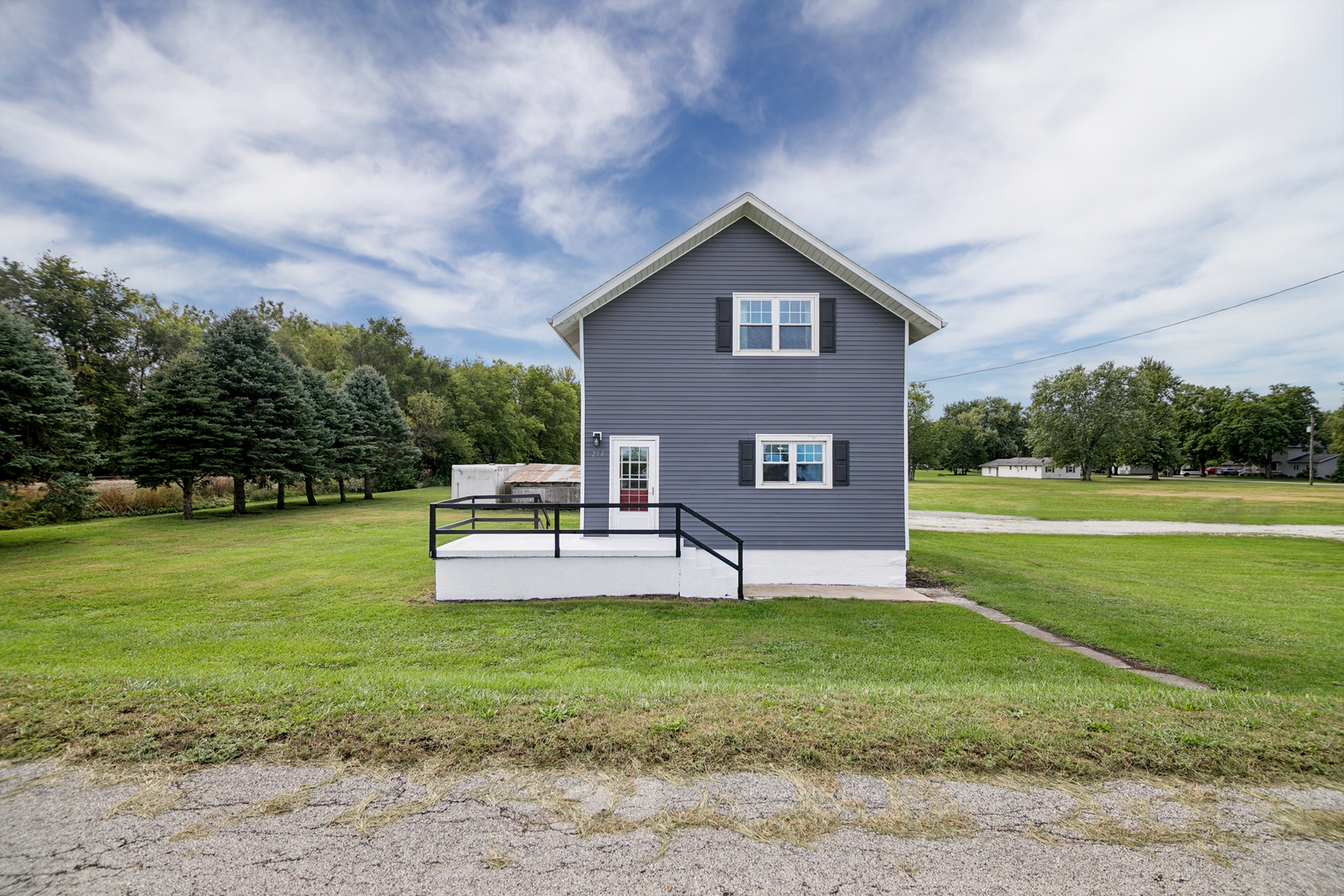 Gray two-story house with a small raised deck and broad grassy lawn.