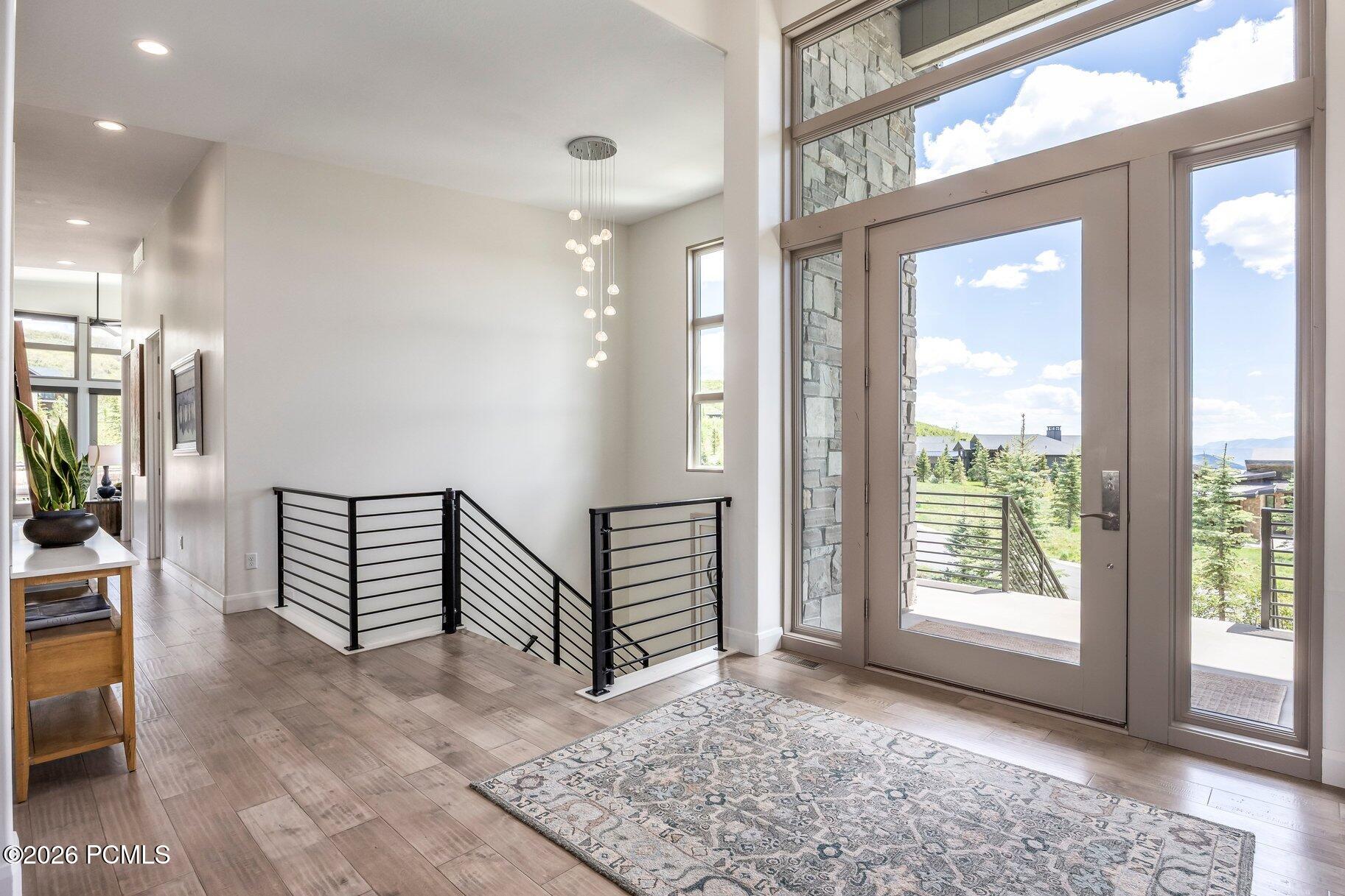 Entry foyer with tall windows, a glass front door, patterned rug, and black metal stair railing.