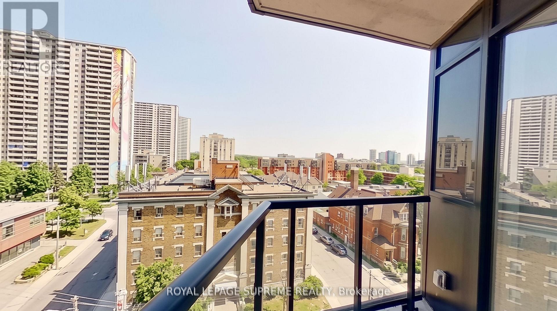 Condo balcony overlooking Toronto apartment buildings and tree-lined streets, framed by a black railing.