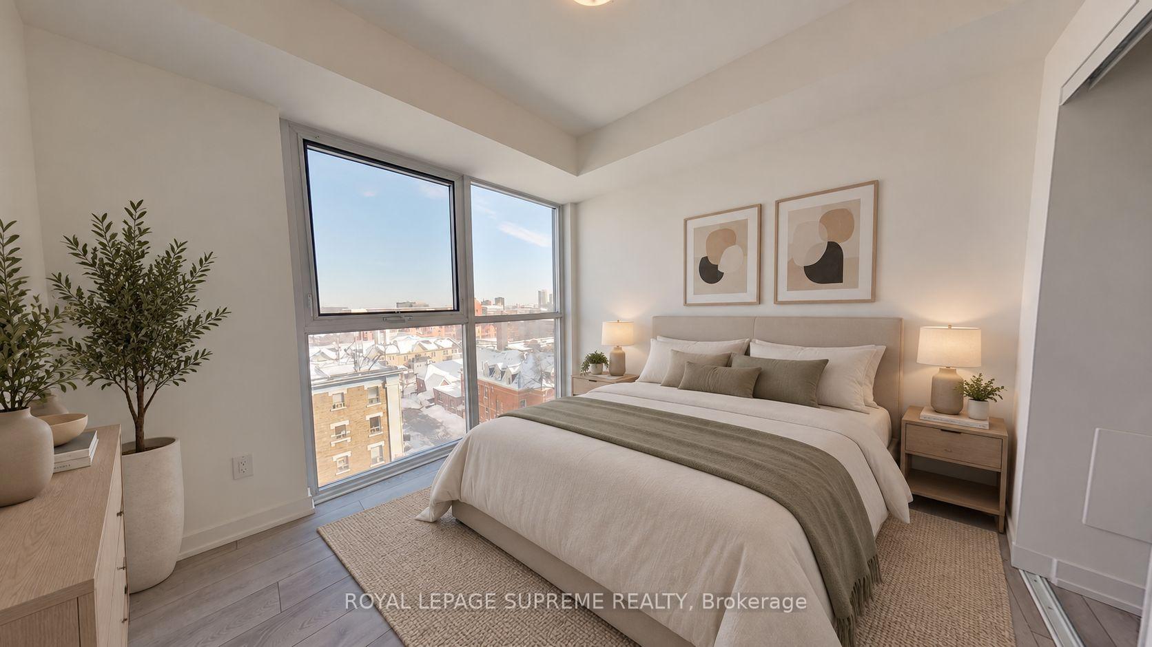 Staged condo bedroom with a large neutral bed beside corner windows overlooking snowy city rooftops.