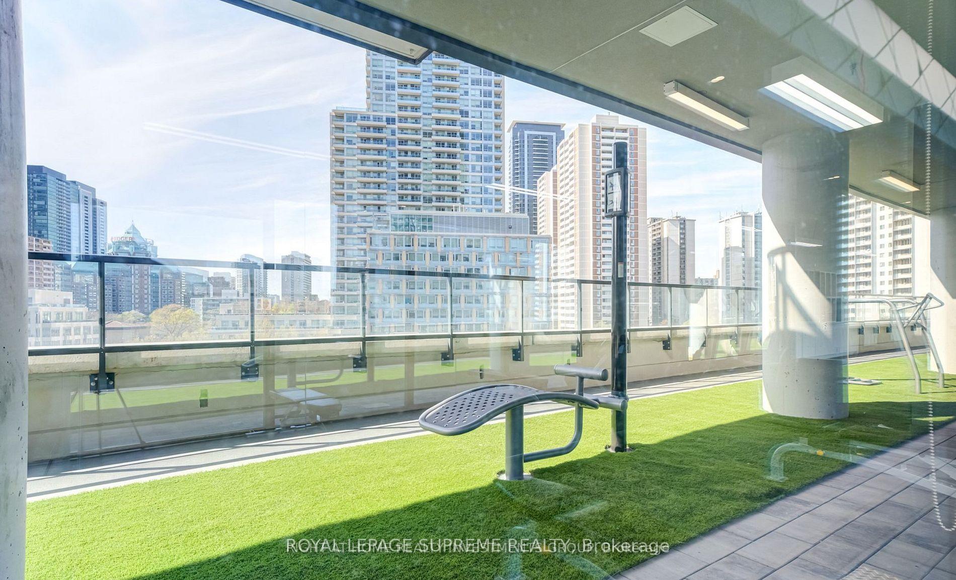 Rooftop terrace with artificial turf, outdoor exercise equipment, glass railings, and a city skyline.