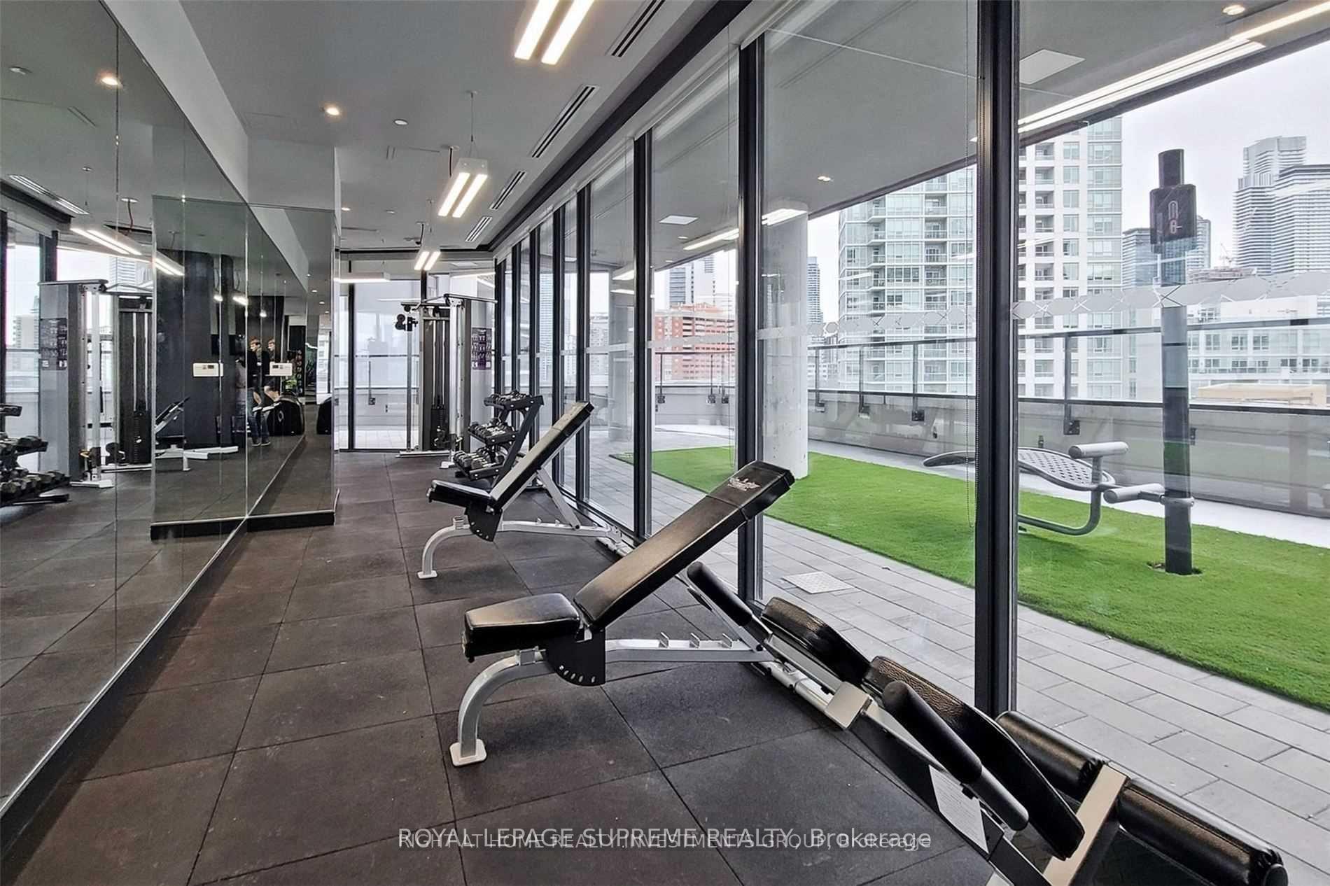 Condominium gym with weight equipment, mirrored walls, and windows overlooking a terrace and Toronto skyline.