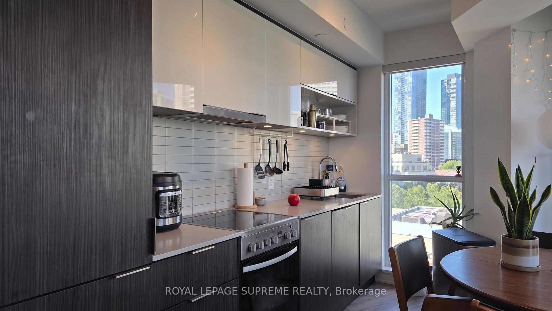 Modern condo kitchen with dark cabinetry and a dining nook by a window overlooking Toronto towers.