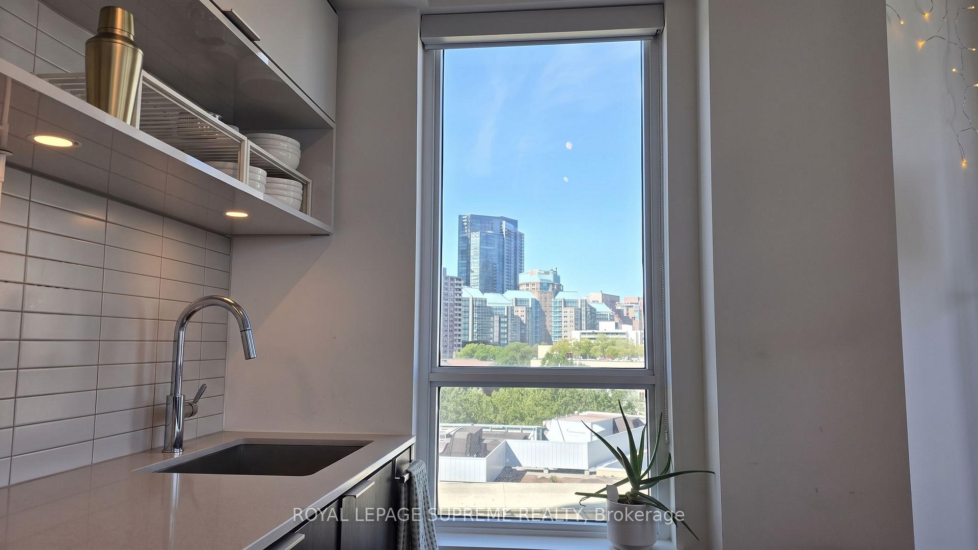Condo kitchen with open dish shelves and a large window overlooking the Toronto skyline.