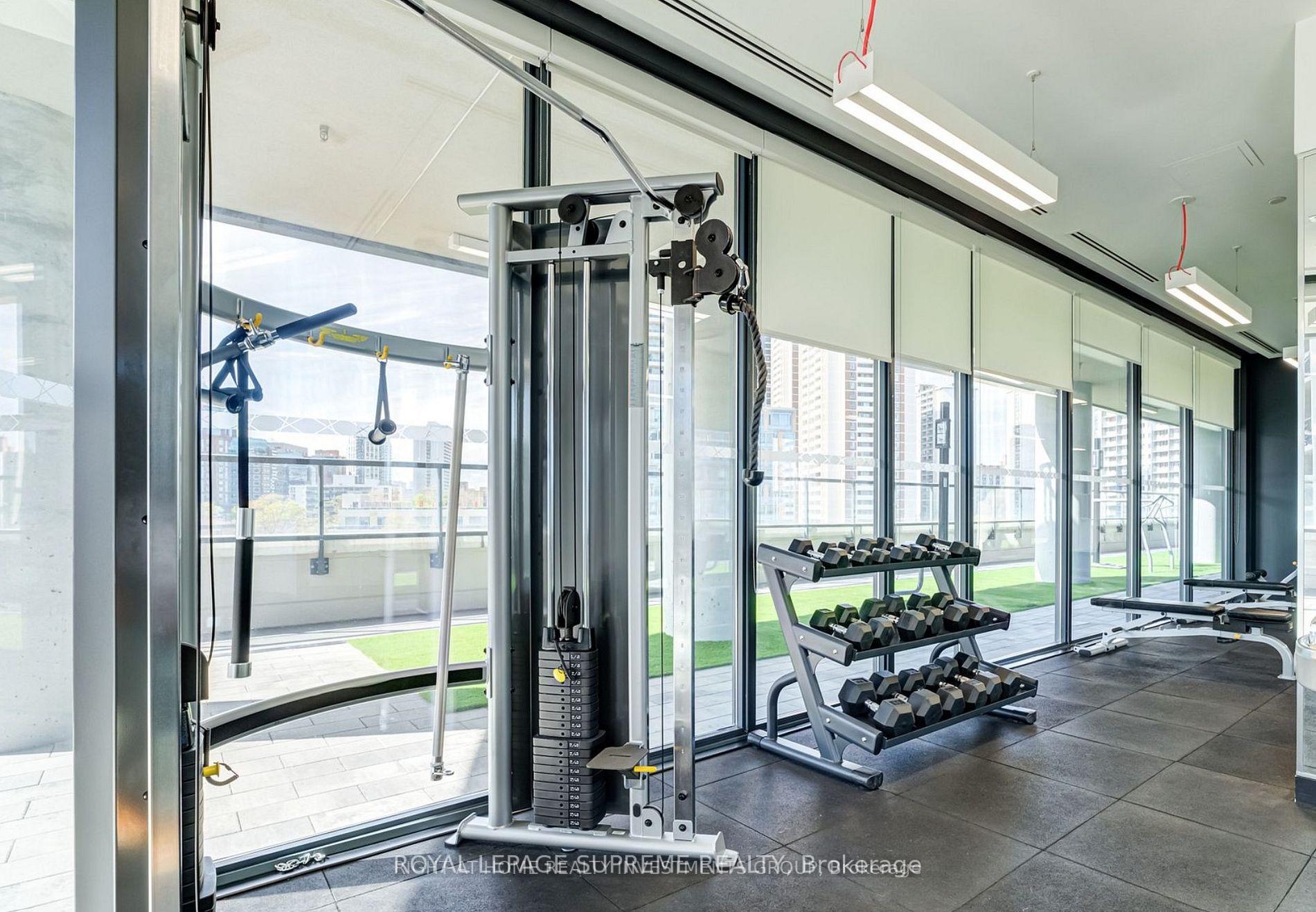 Condo fitness room with cable machine and dumbbell racks beside floor-to-ceiling windows.