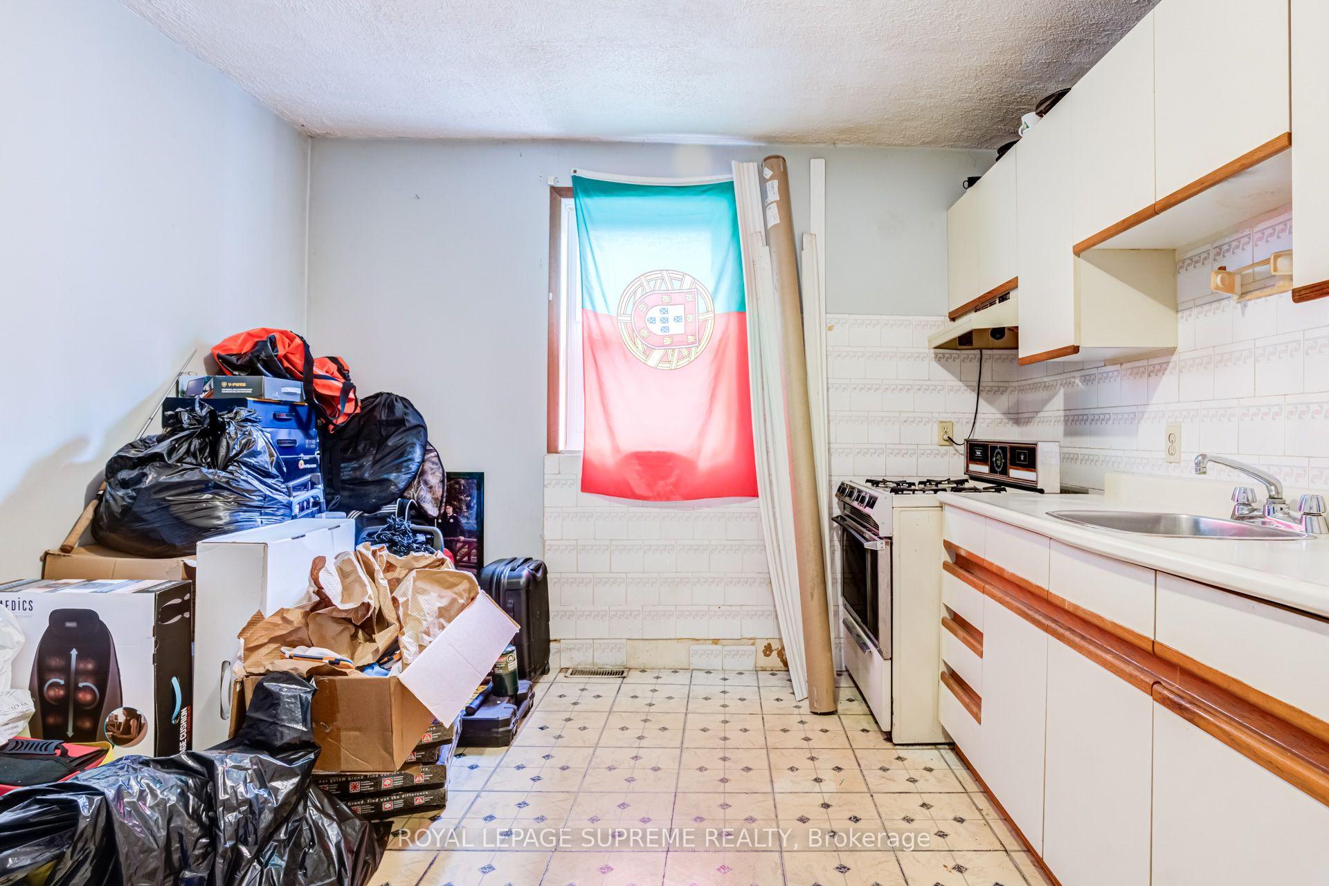 Cluttered kitchen with cream cabinets, a gas stove, and a Portuguese flag covering the window.