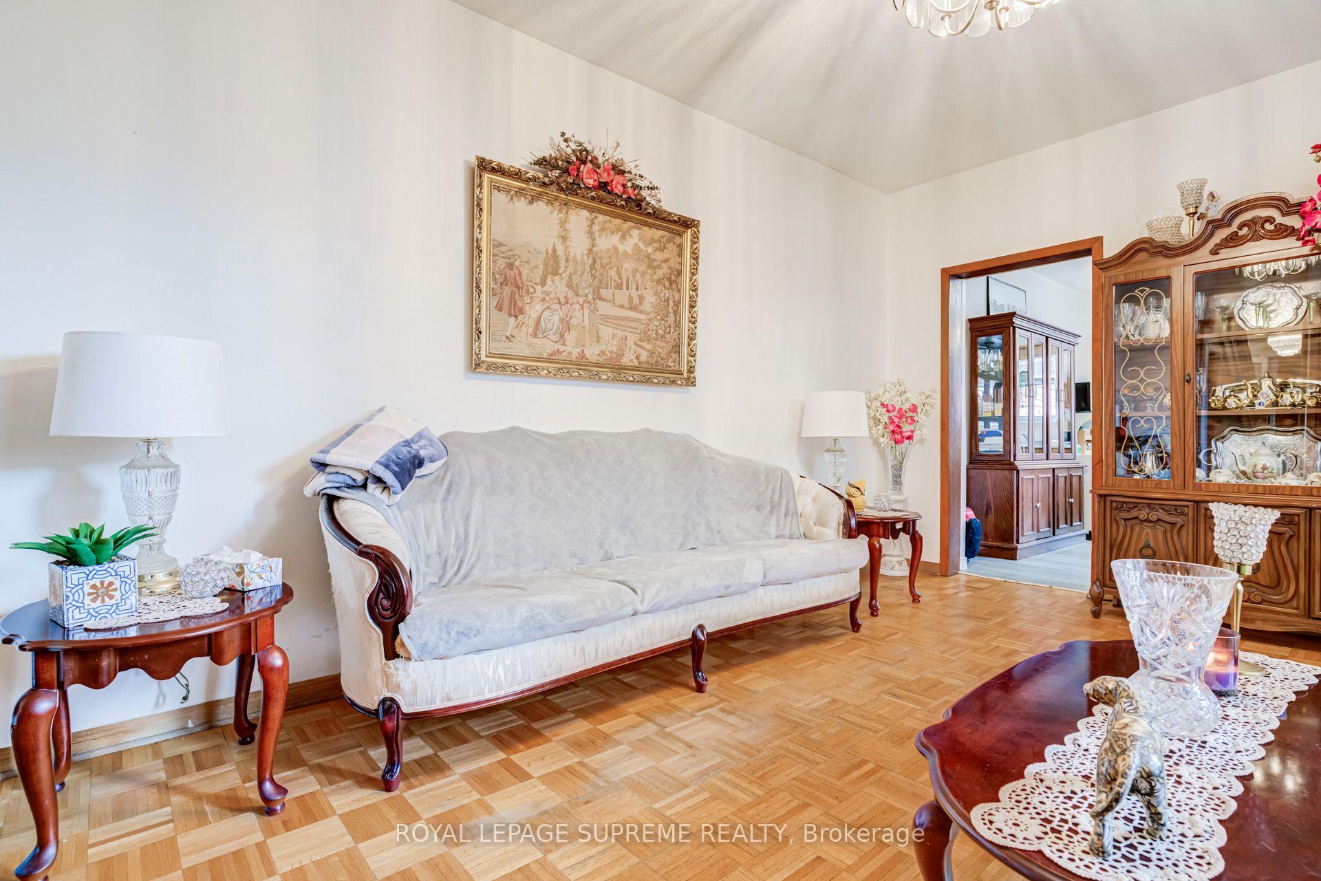 Living room with a white-covered sofa, parquet flooring, and an ornate wooden china cabinet.