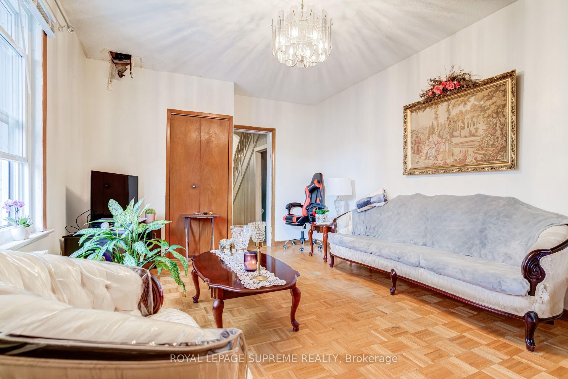 Living room with parquet flooring, a chandelier, two sofas, and a damaged patch near the ceiling.