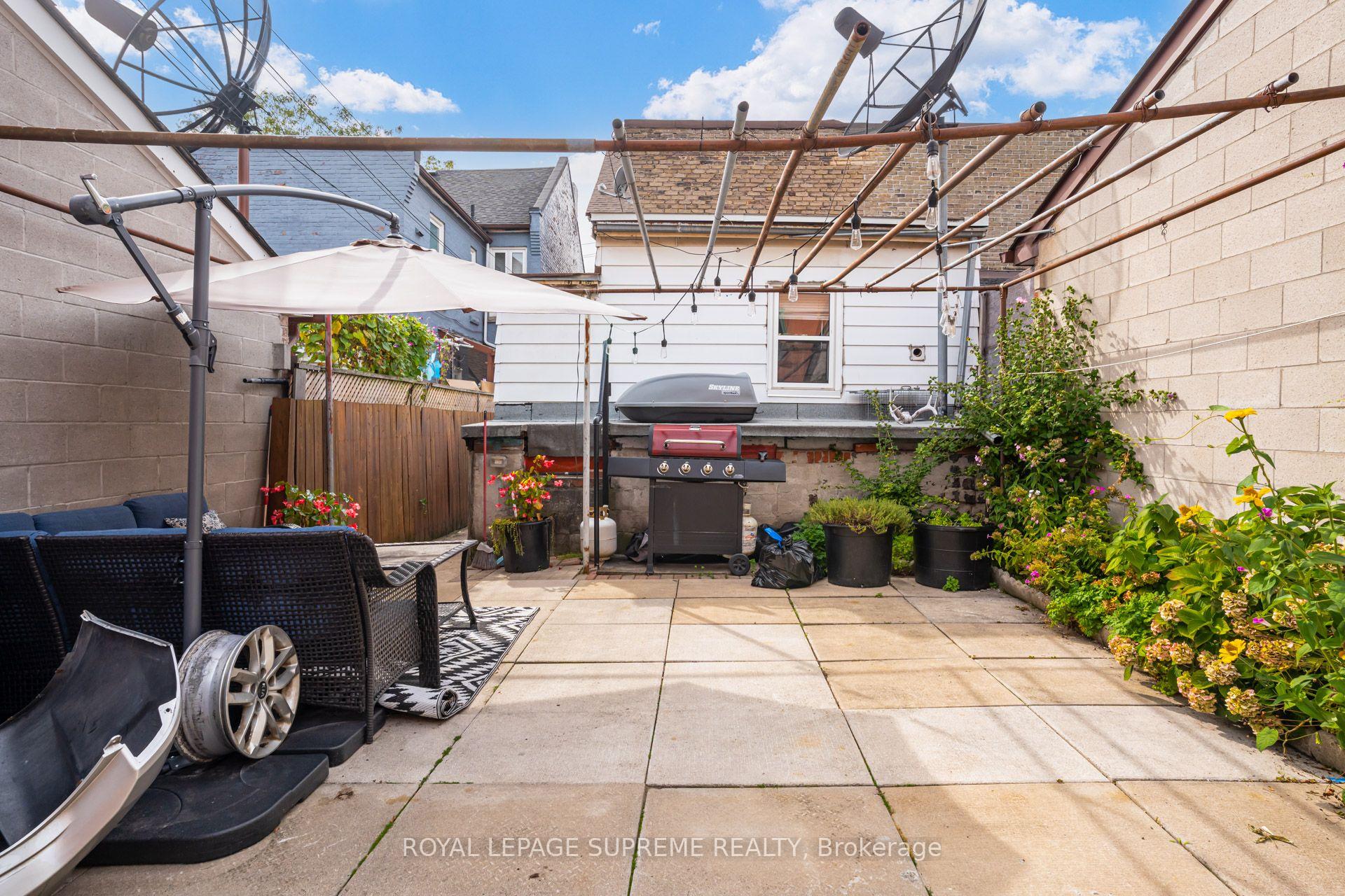 Backyard patio with umbrella seating, barbecue grill, potted flowers, and overhead string lights.