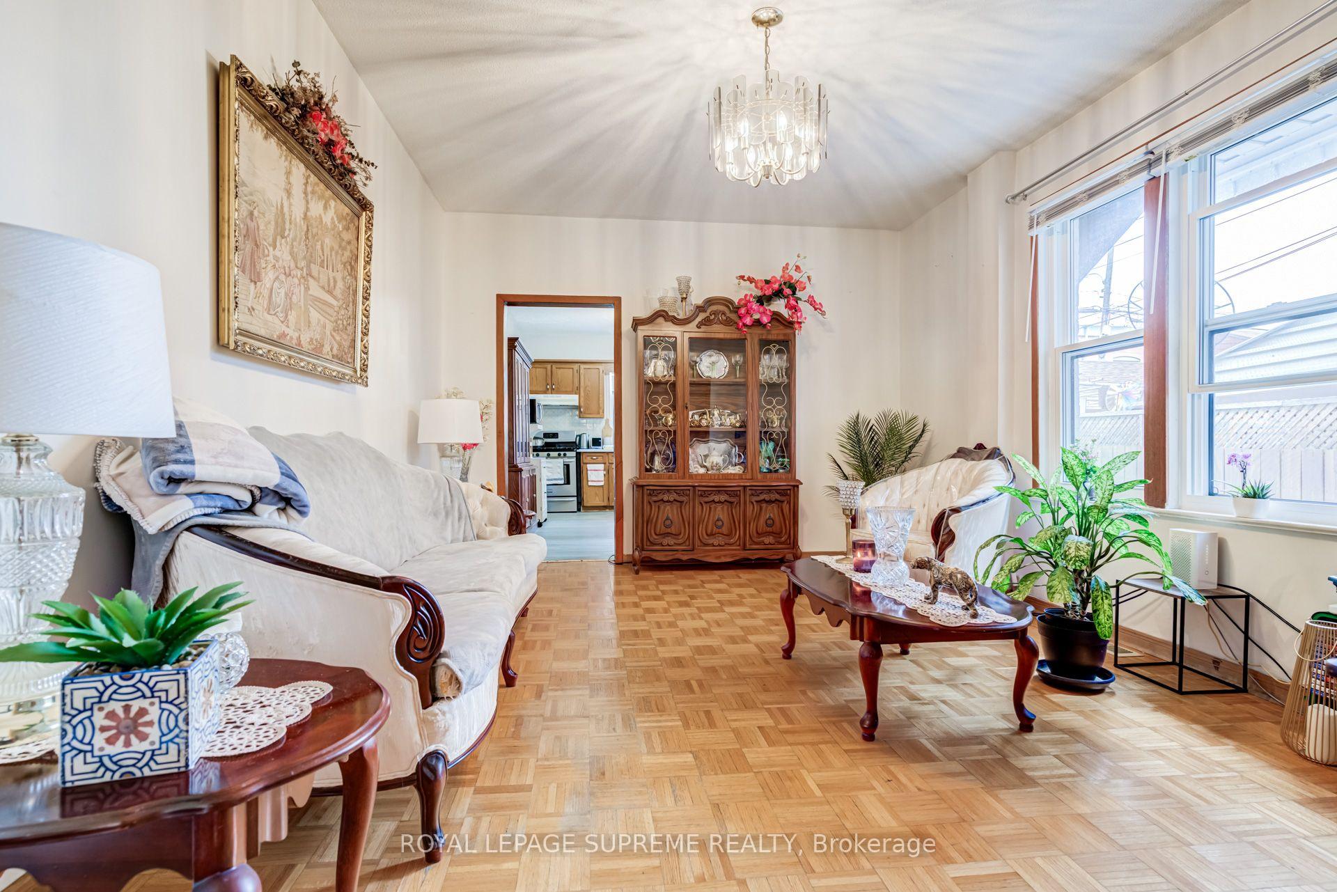 Living room with parquet flooring, cream sofas, a carved china cabinet, and large windows.