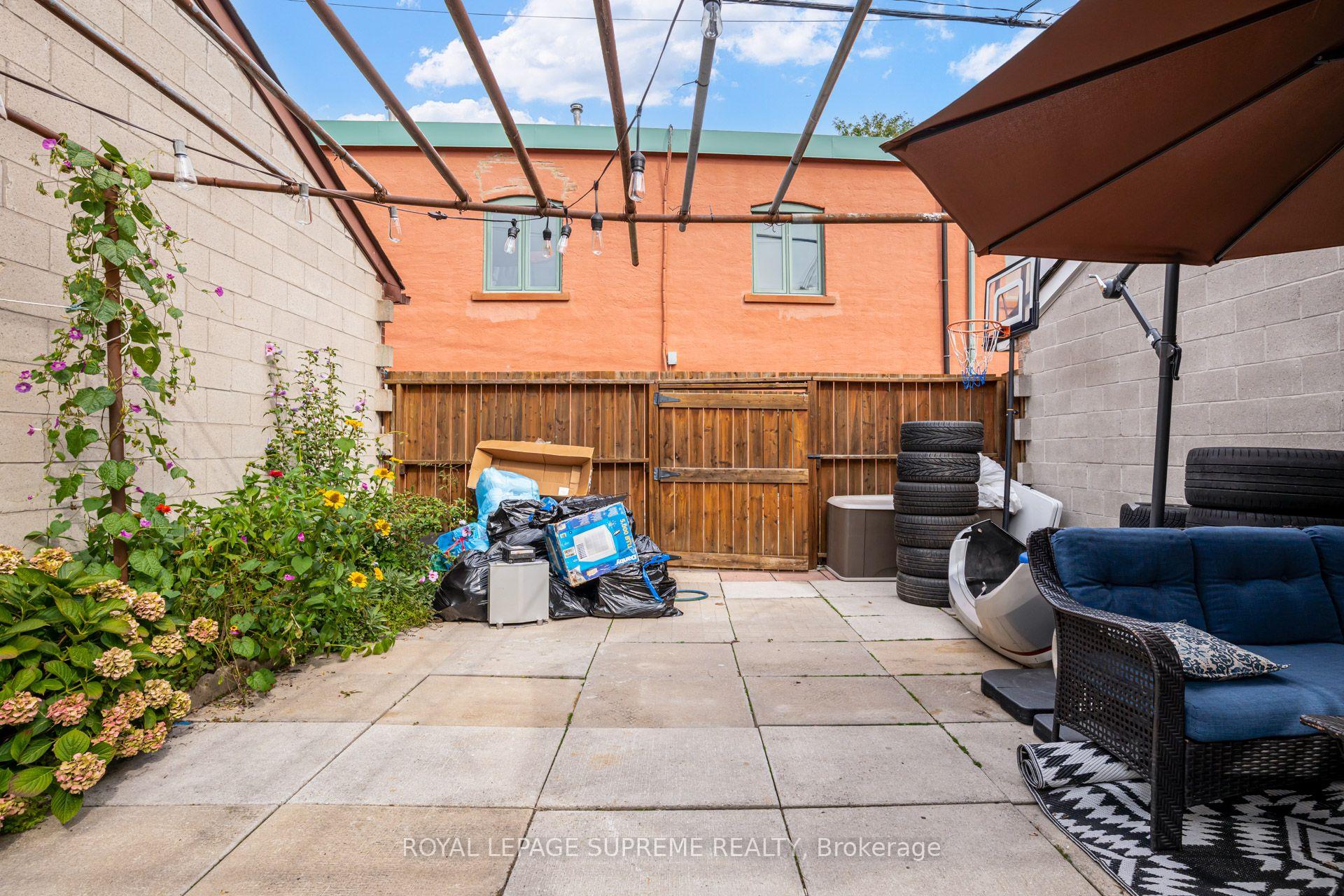 Backyard patio with a large umbrella, string lights, flower beds, and a wooden gate.