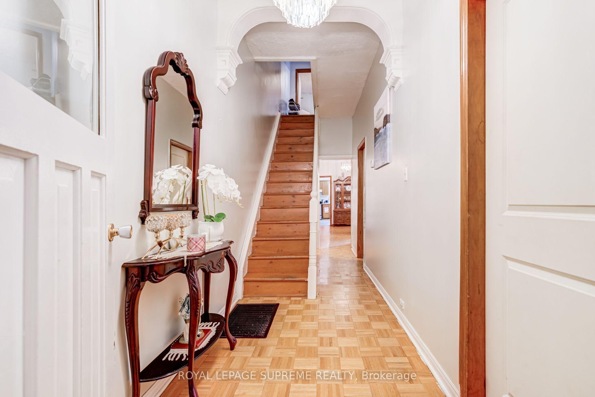 Entry hall with a wooden staircase, parquet flooring, and a carved console table beneath a mirror.