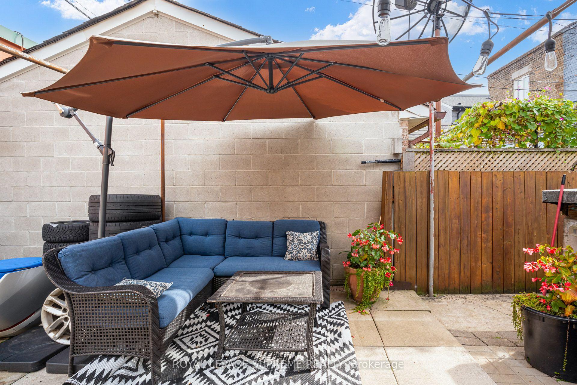 Backyard patio with blue wicker seating beneath a large brown umbrella and flowering plants.