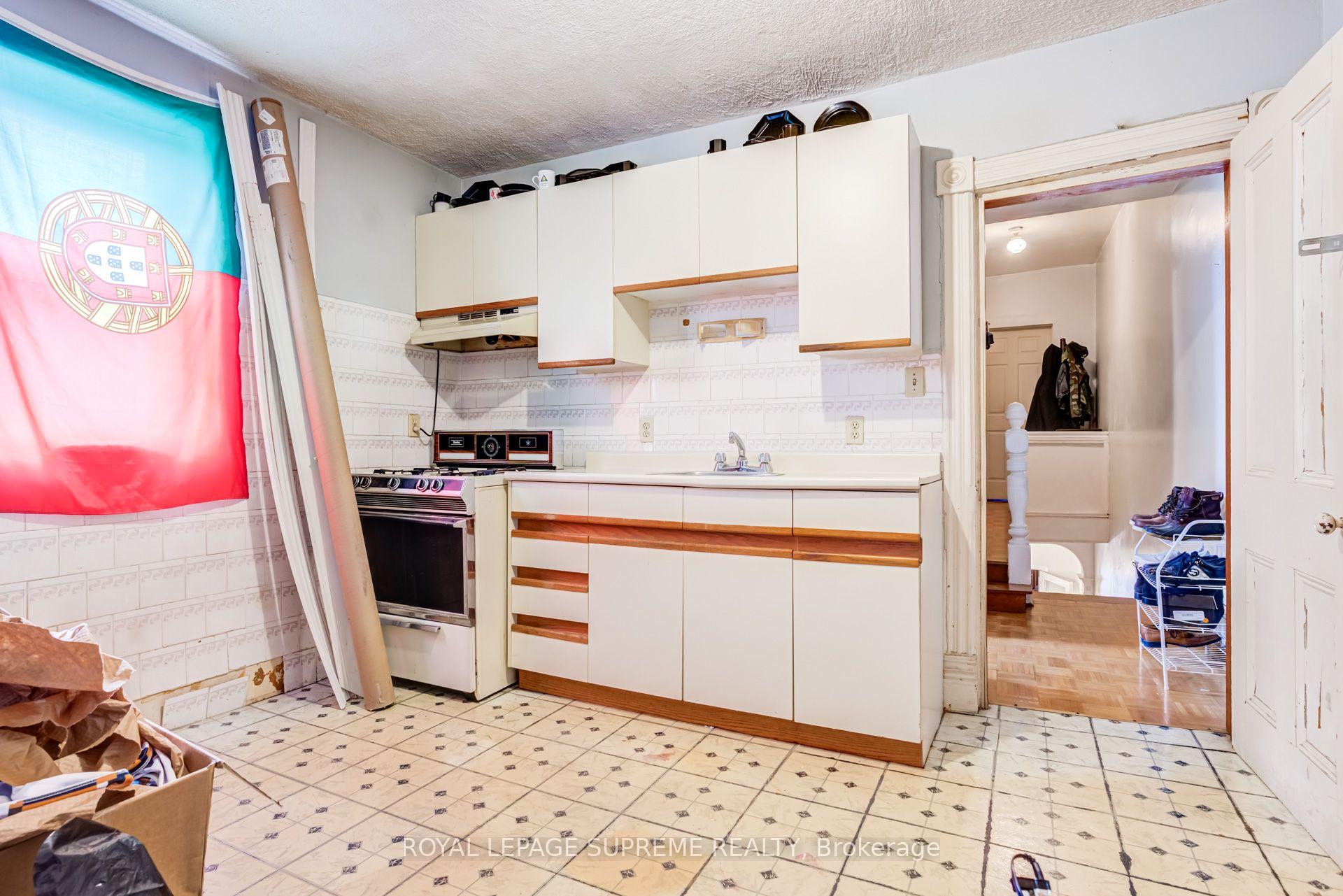 Kitchen with white wood-trimmed cabinets, patterned tile, and a doorway to a cluttered hallway.