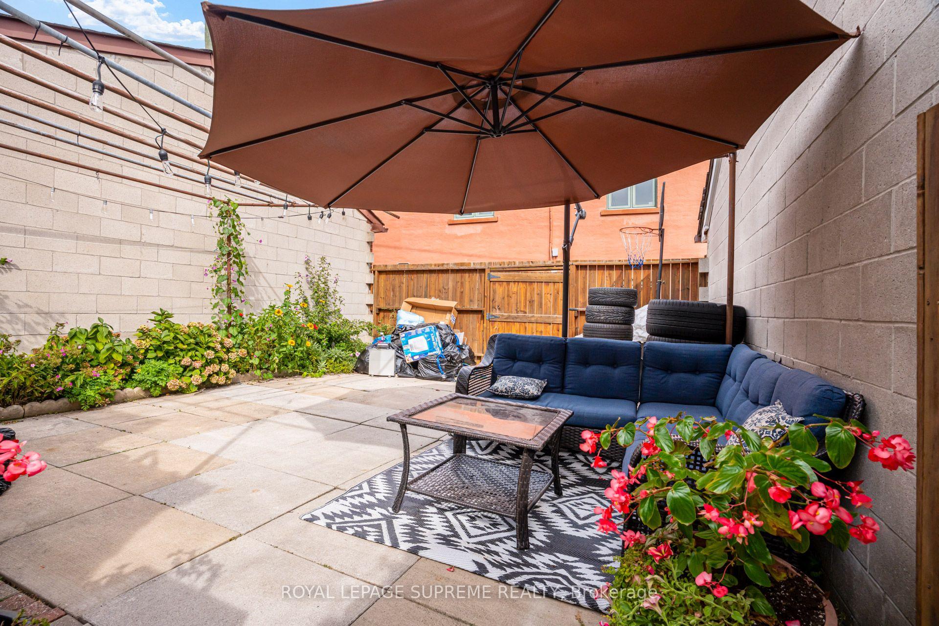 Backyard patio with a navy sectional, large umbrella, paved seating area, and flowering garden beds.