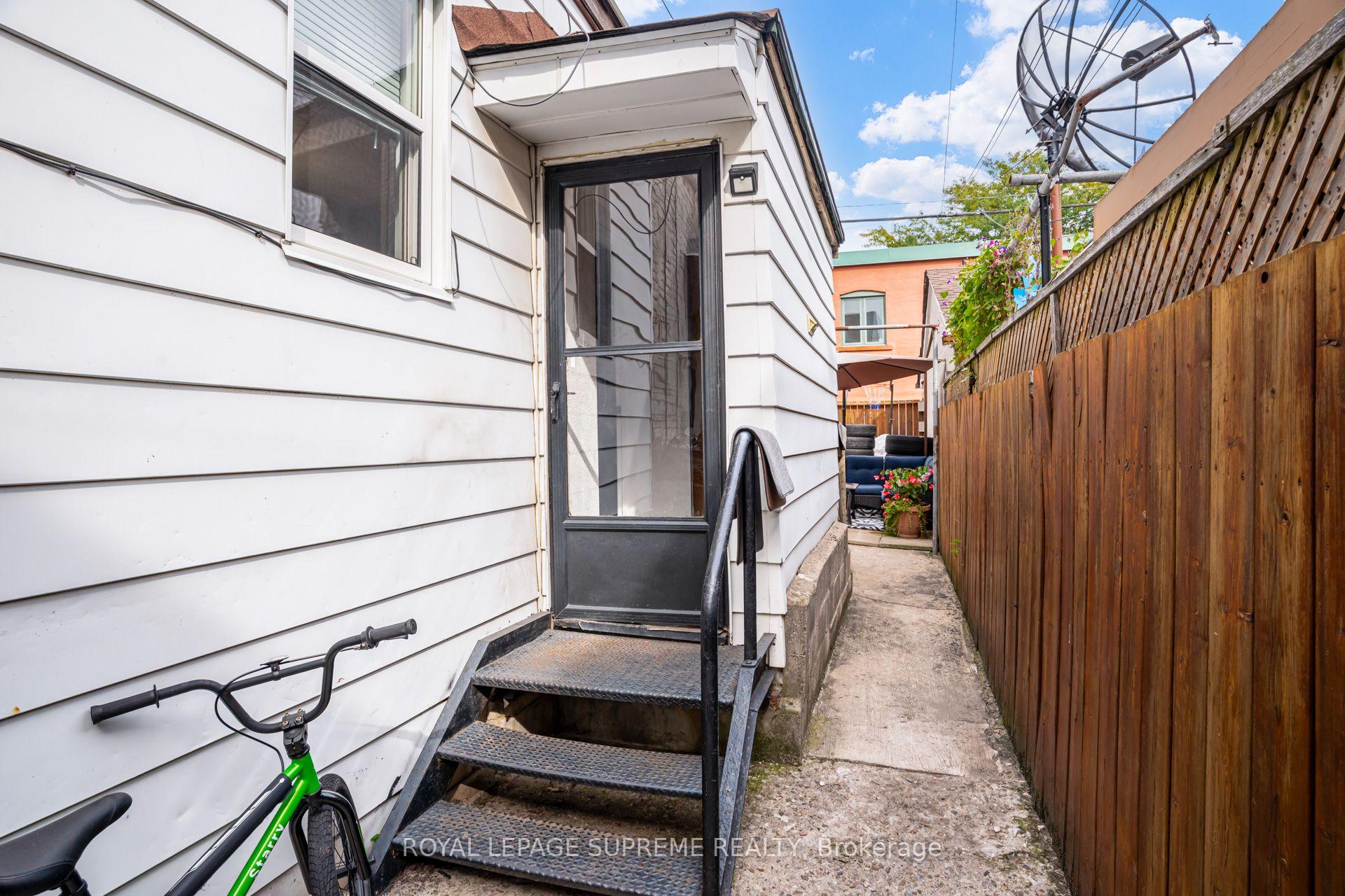 Side entrance of a white-sided home with metal steps, a narrow fenced walkway, and a bicycle.