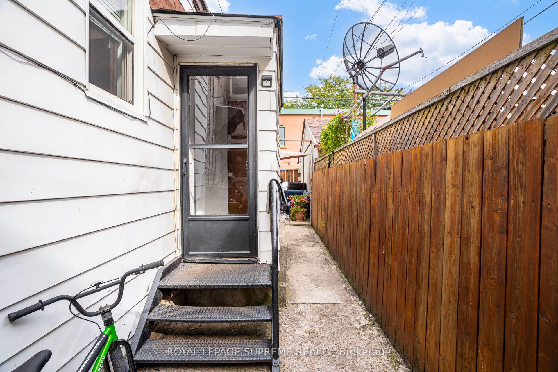 House side entrance with metal steps, a narrow walkway, and a tall wooden fence.