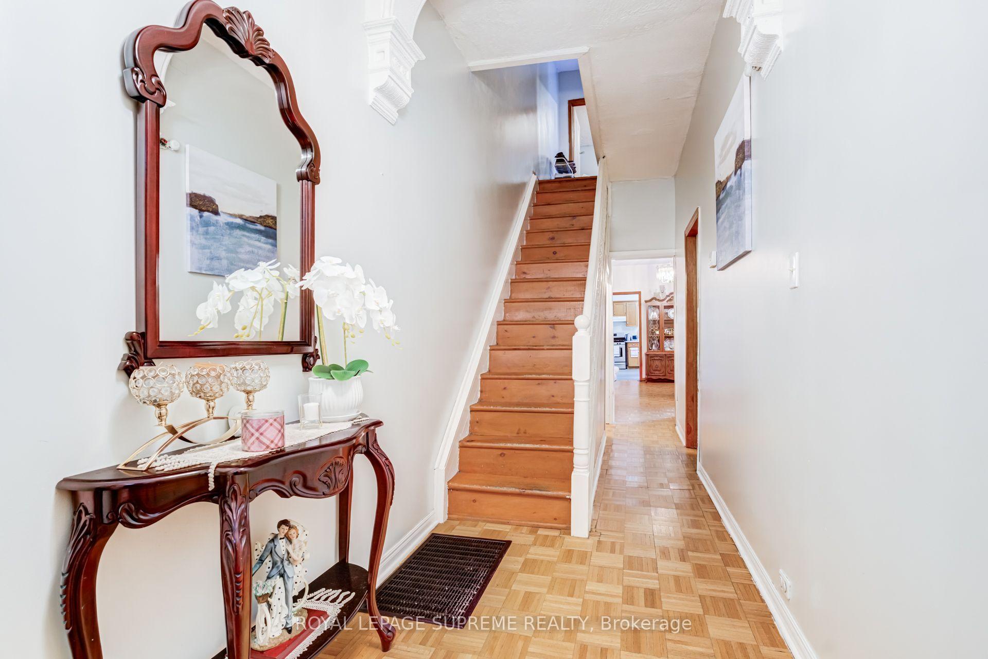 Hallway with a wooden staircase, parquet flooring, and a carved console table with a mirror and orchids.