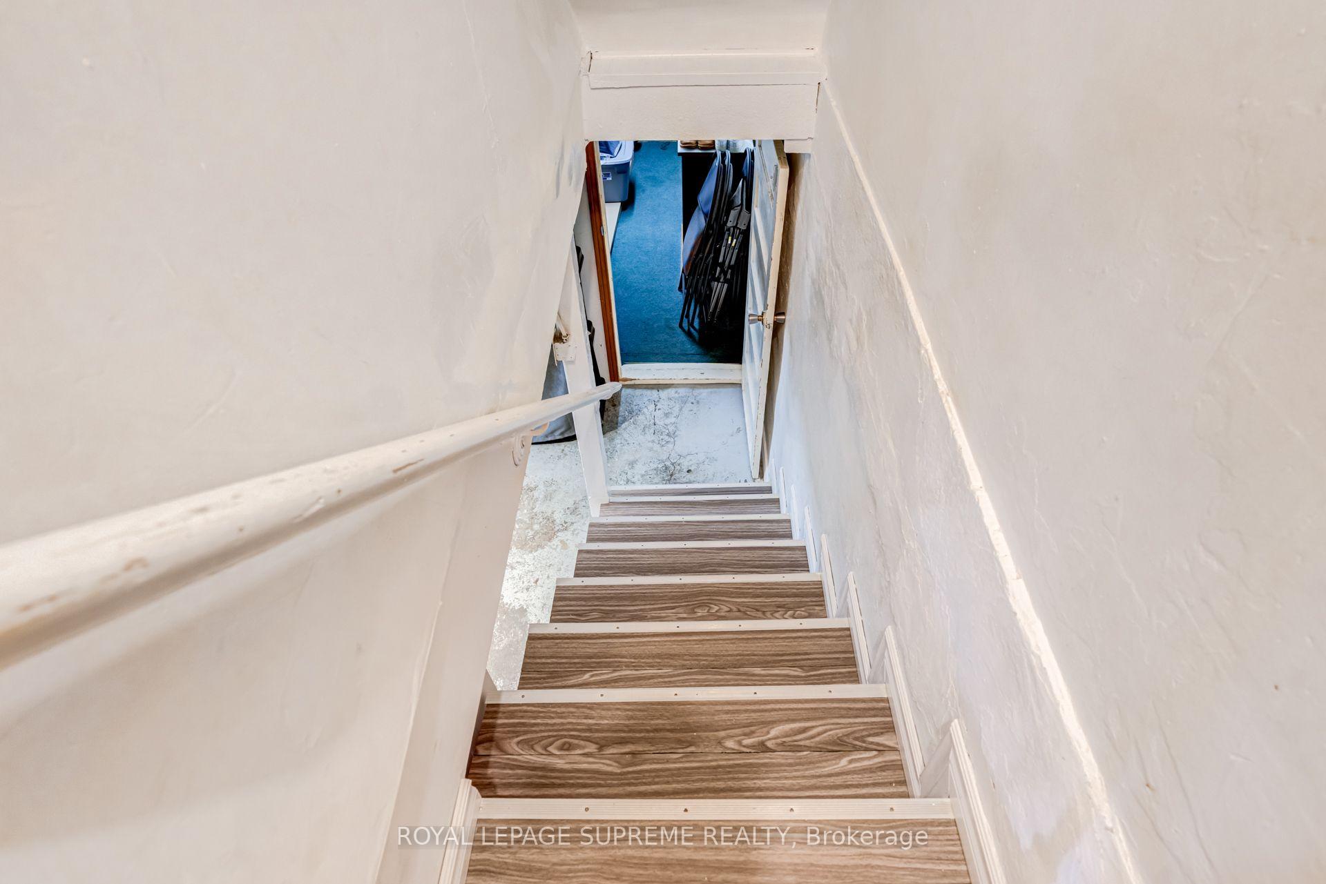Staircase descending to a blue-carpeted room, with wood-look treads and white walls.