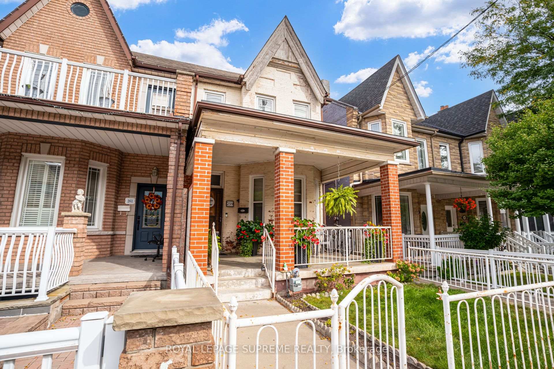 Toronto row house with a covered brick-column porch, white railings, steep gables, and flower-filled planters.